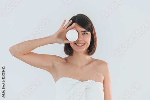 Holding cream for the skin care. Young brunette is indoors against white background