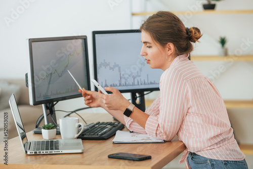 Using smartphone. Female stock broker in casual clothes is working in the office by pc