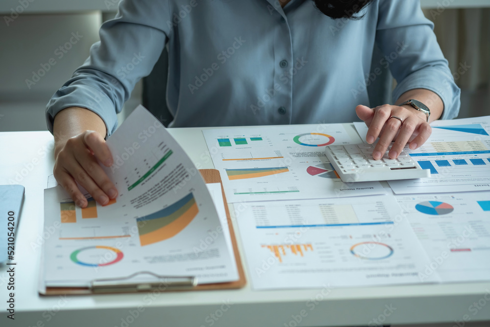 Portrait of a female accountant using a calculator and laptop to calculate balance using graphs for customers. Portrait of a female accountant using a calculator and laptop to calculate balance using graphs for customers.