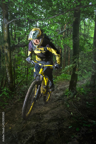 Man, cyclist in the full face helmet uphill on the yellow enduro bicycle in the green forest