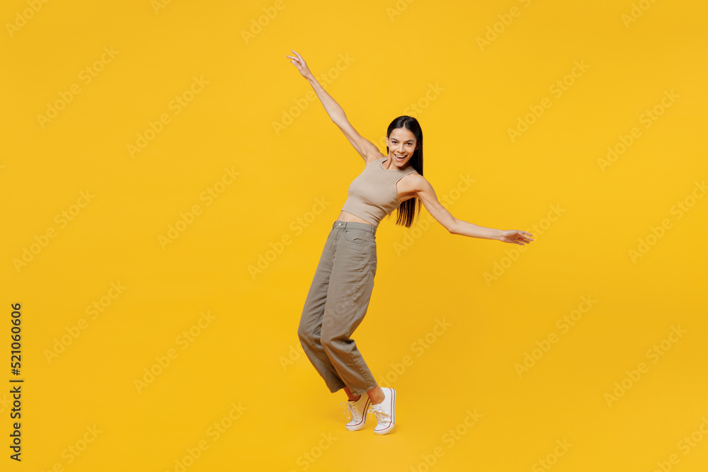 Full body young latin woman 30s she wear basic beige tank shirt stand on toes leaning back dance with outstretched hands isolated on plain yellow backround studio portrait. People lifestyle concept. Full body young latin woman 30s she wear basic beige tank shirt stand on toes leaning back dance with outstretched hands isolated on plain yellow backround studio portrait. People lifestyle concept.