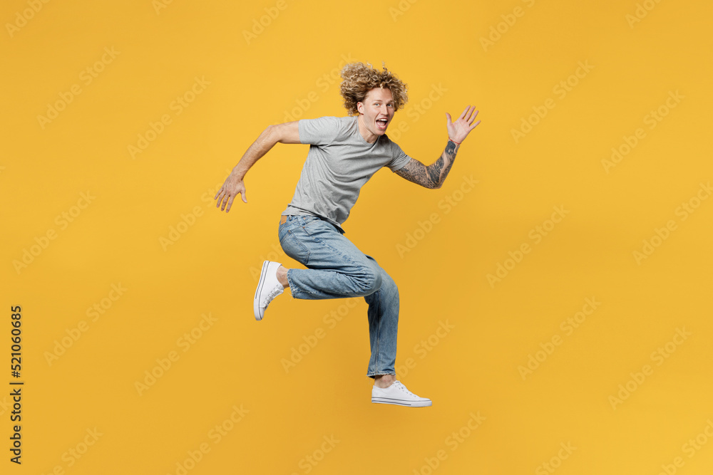 Full body side view young strong sporty caucasian man 20s he wear grey t-shirt look camera jump high run fast look camera isolated on plain yellow backround studio portrait. People lifestyle concept.