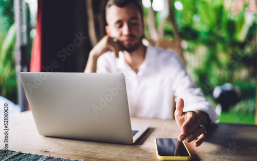Blurred male content manager checking received notification on digital cellphone while working remotely on laptop technology  graphic designer with netbook using mobile phone for chatting