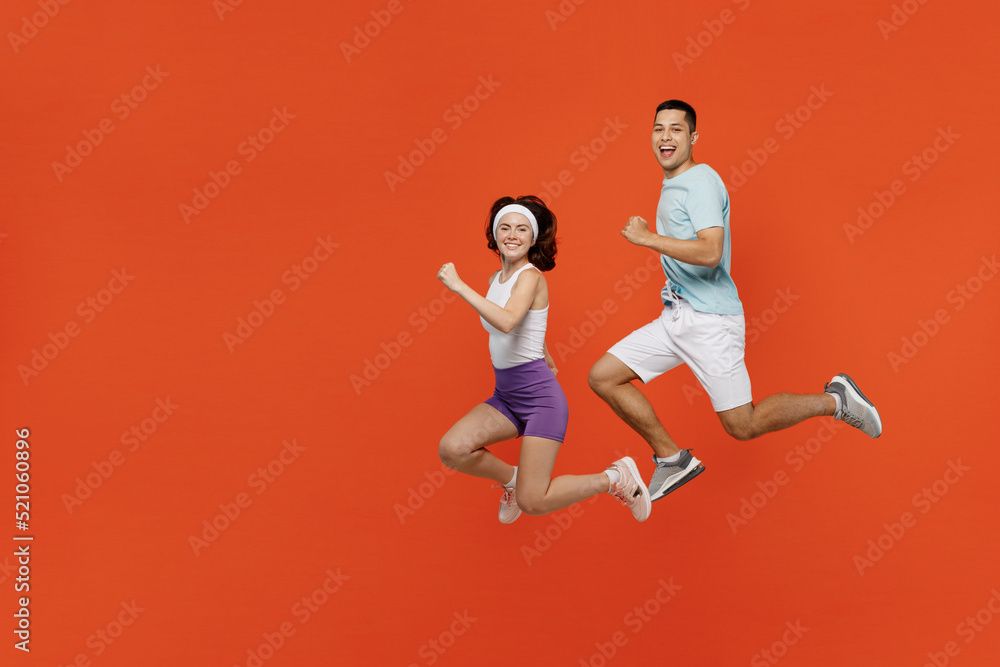 Full body side view young fitness trainer instructor sporty two man woman in headband t-shirt jump high run spend weekend in gym isolated on plain orange background. Workout sport lifestyle concept.