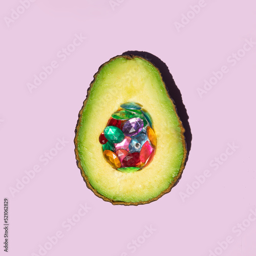 Creative exotic fruit composition. Avocado with colorful shiny gemstones as core on pastel light purple background. Minimalistic nature concept. Healthy food concept.