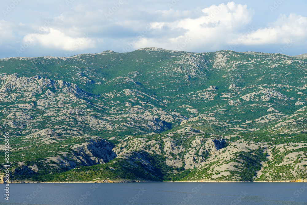 A mountain overgrown with green vegetation above the blue sea and under the cloudy sky
