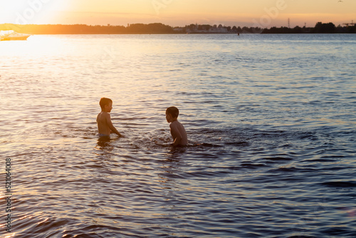 Children boys swimming in the river or lake at sunset, dark silhouettes of children in the water on the beach