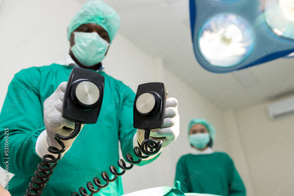 The doctor is giving a defibrillators to save the patient's life in the hospital. CPR. Using a defibrillator to save lives. Hands of man surgeon holding defibrillator at the hospital - obrazy, fototapety, plakaty 