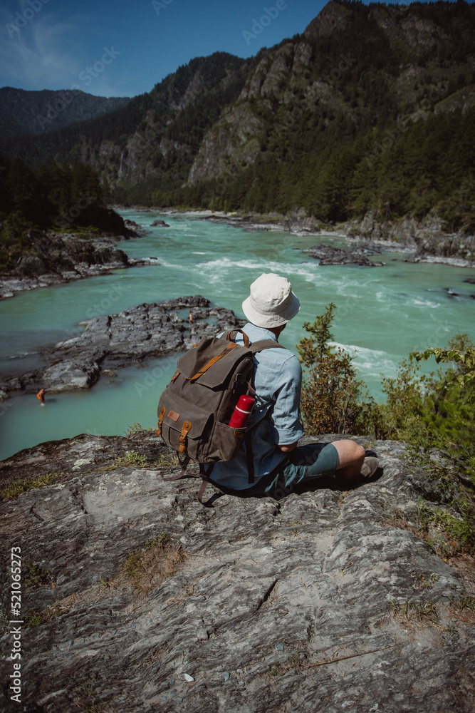 hiker men with backpack sitting in the mountains in sunny day. male tourist looking at katun river in Altai mountains