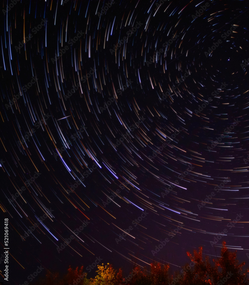 Star trails in the night sky with long exposure. Movement of stars over the Earth. Lines of colored stars. Polar Star. Starry background