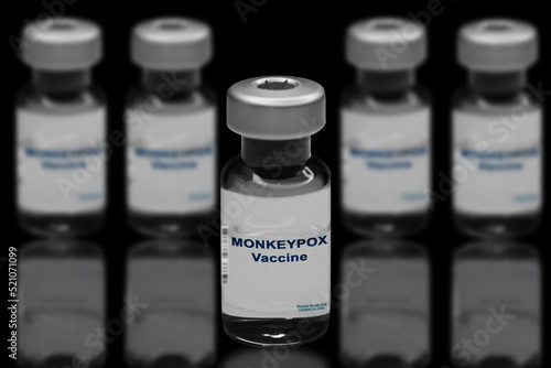 Monkeypox vaccine close-up on a black mirror background. In the background are blurred vaccine vials