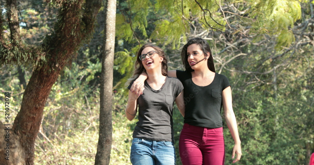 Two girlfriends together walking at the park embracing each other Two girlfriends together walking at the park embracing each other