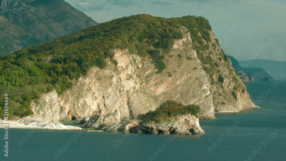 Top view of beautiful cliffs of mountains by sea on sunny day. Creative. Beautiful landscape with rocky shore and green trees. Seashore with rocks and greenery on warm day