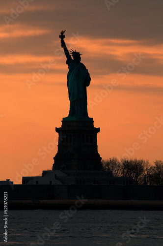Silhouette of Statue of Liberty against a vivid orange sunset sky concept for NYC landmarks, American patriotism and symbol of freedom in America © Victor Moussa