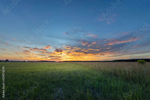 Rural landscape with colorful clouds and sun on the horizon. Bright sunset.