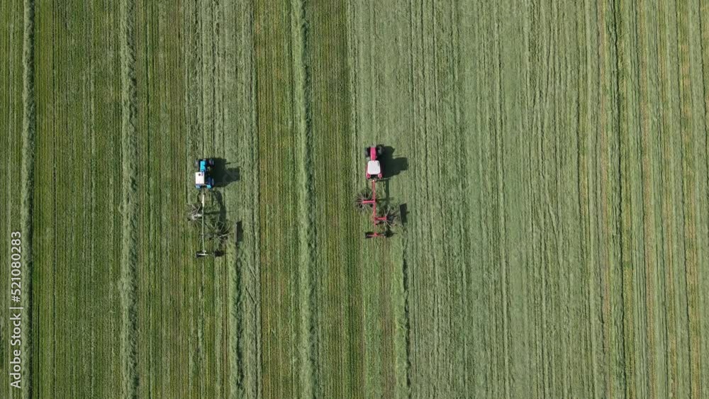 Tractors raking cut meadow grass after wilting. Silage making processes for winter cattle feed Tractors raking cut meadow grass after wilting. Silage making processes for winter cattle feed