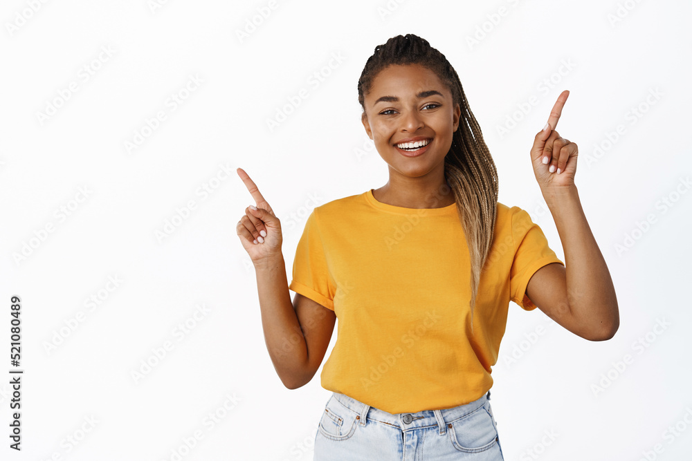 Happy smiling young millennial girl pointing fingers sideways, showing two ways, variants of promo offers, standing over white background Happy smiling young millennial girl pointing fingers sideways, showing two ways, variants of promo offers, standing over white background