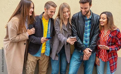 Friends standing by a wall background and using their smarphones - Young people on social media