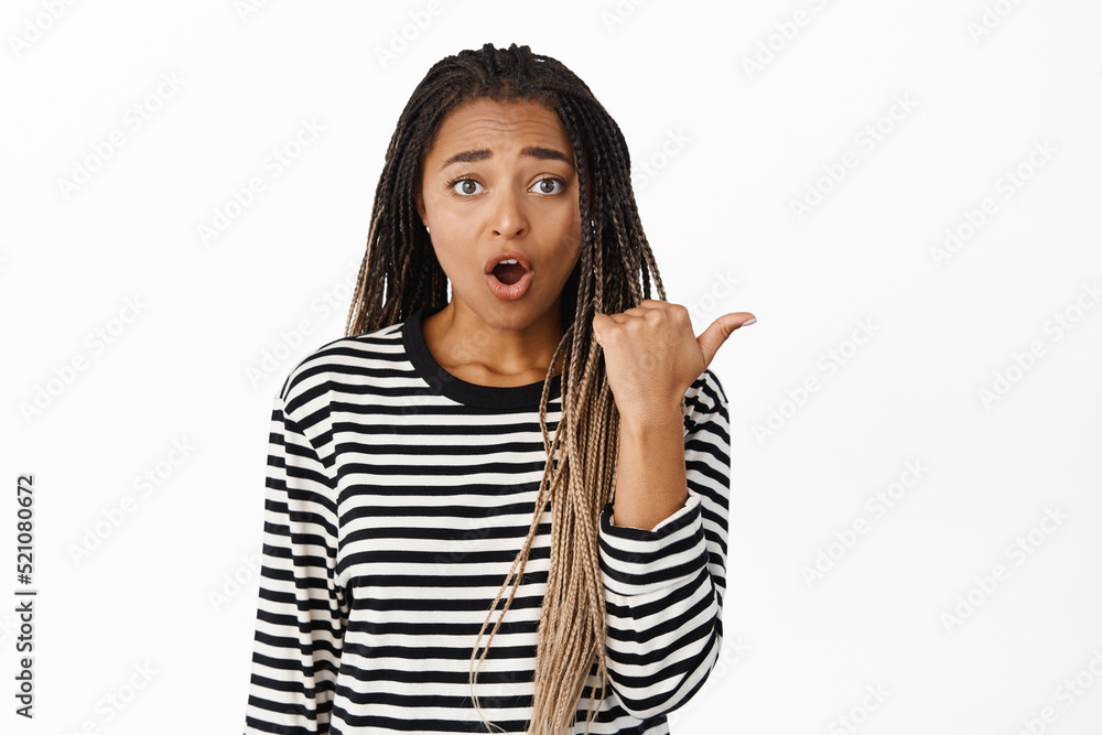 Shocked black girl pointing finger aside and looking concerned, worried about smth happening to the right, standing over white background Shocked black girl pointing finger aside and looking concerned, worried about smth happening to the right, standing over white background