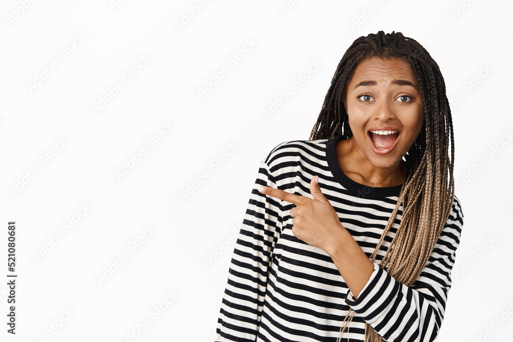 Hey look there. Excited Black teenage girl pointing finger away and showing banner, smiling happy, demonstrating logo or sale offer, white background Hey look there. Excited Black teenage girl pointing finger away and showing banner, smiling happy, demonstrating logo or sale offer, white background