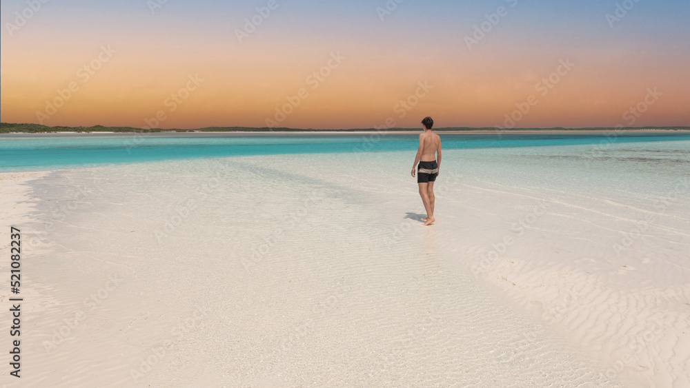 Young man  standing from behind on tropical white sand beach in Caribbean looking over the perfect turquoise ocean. Luxury living vacation destination.