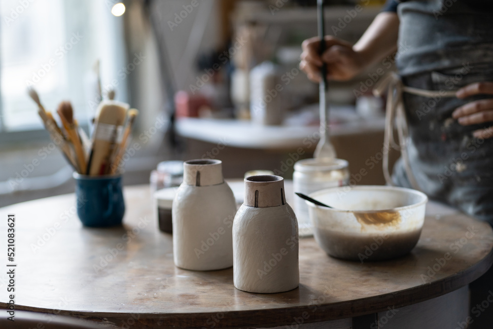 Crop photo of skilled master leaving clay vases to dry out on table after baking and handmade shaping in studio. Craftsworker hands put necessary appliances for painting vase on table in special shop Crop photo of skilled master leaving clay vases to dry out on table after baking and handmade shaping in studio. Craftsworker hands put necessary appliances for painting vase on table in special shop