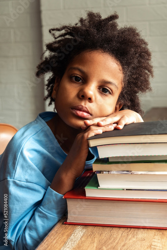 Sad tired African-American girl doing homework at home puting her head on a stack of textbooks.Back to school concept.School distance education home schooling diverse people.