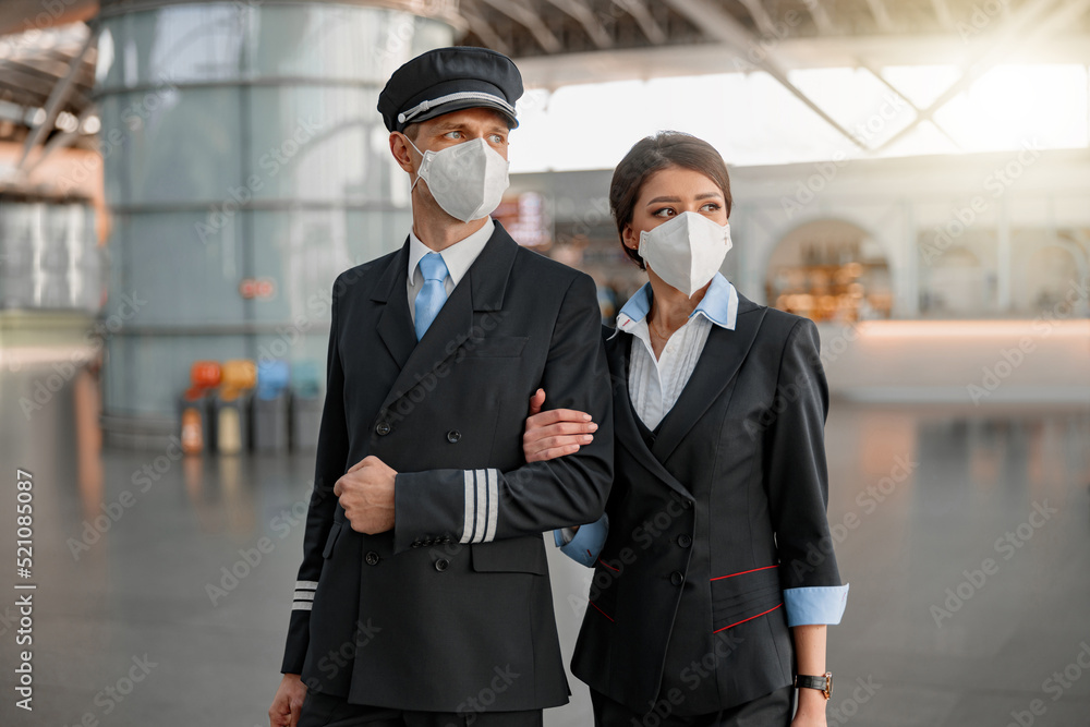 Fototapeta premium Stewardess and pilot in protective masks looking away in the terminal