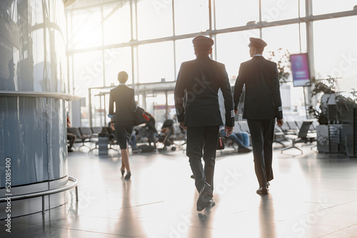 Two pilots walking along the airport terminal following the stewardess