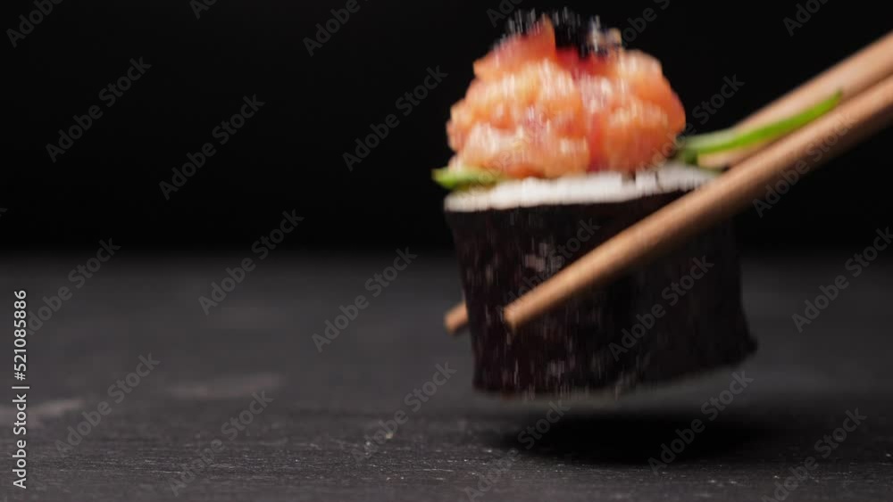 Take one sushi roll from black slate board using chopsticks, Closeup Take one sushi roll from black slate board using chopsticks, Closeup