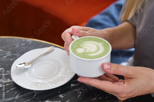 Woman with a cup of matcha latte sits in the cafe. Delicious green matcha tea in a green cup close-up. Japanese hot milky beverage. Healthy Matcha Tea Made with Organic Ingredients