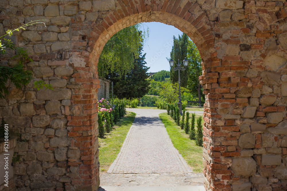 Brickstone arch and passage  in Fortunago, one of the most charming villages of Oltrepò Pavese, Lombardia countryside, Italy. Green park in the background.