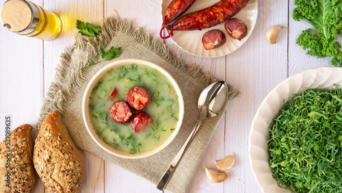 Table with Portuguese-style soup called Caldo Verde and bread, Cabbage julienne, oil, and chorizo sausage. Flat lay photo