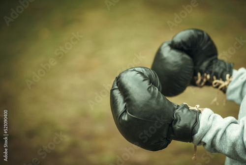 Large black leather boxing gloves on the hands of a child. Training a child in the park. A young boxer.
