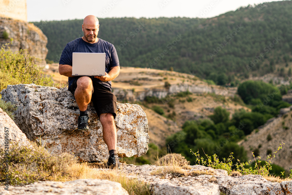 Freelance or digital nomad working with a laptop sitting outdoors on a rock.