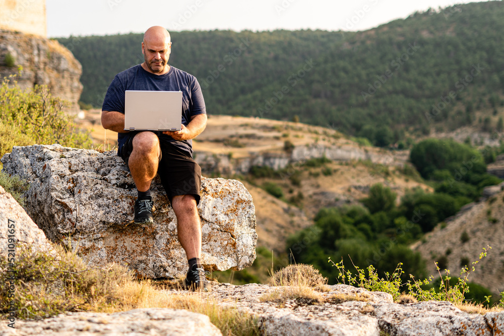 Freelance or digital nomad working with a laptop sitting outdoors on a rock. Freelance or digital nomad working with a laptop sitting outdoors on a rock.