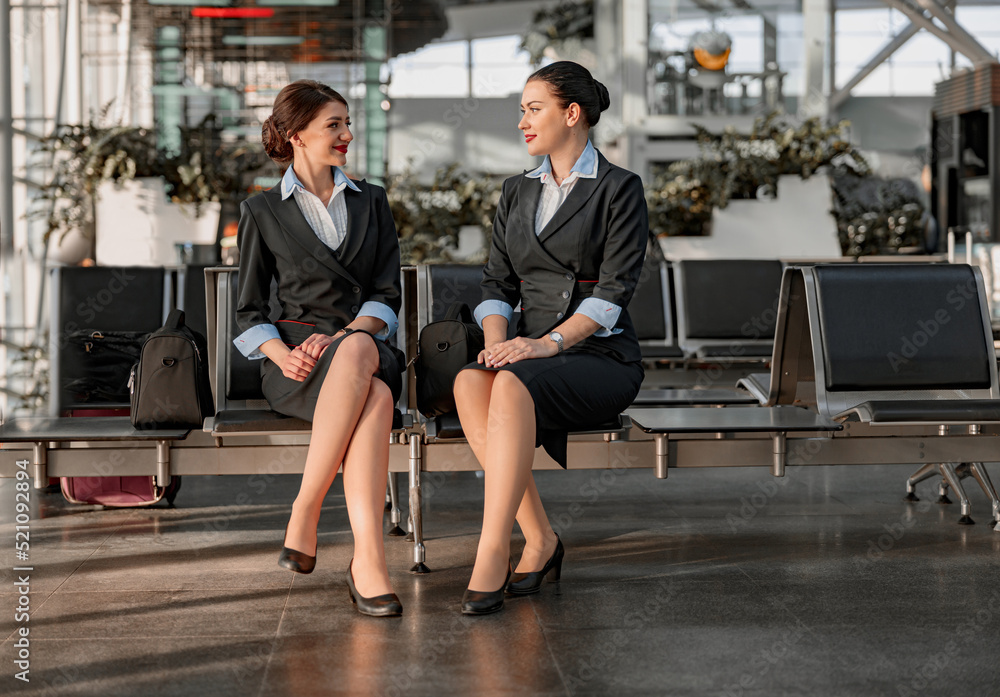 Two flight attendants sitting on the seats and talking in the airport terminal Two flight attendants sitting on the seats and talking in the airport terminal