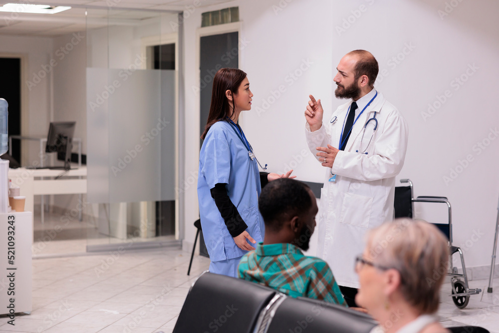 Fototapeta premium Diverse medical team talking about healthcare support in hospital reception, discussing about patients and appointments at medical facility lobby. Doctor and nurse in waiting room area.