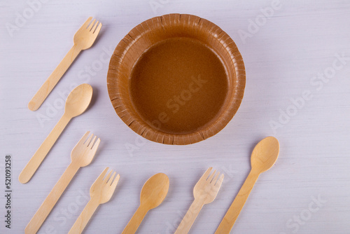 Eco - friendly plate and wooden fork, spoon lay towards paper dish ware on white background. Disposable tableware. Top view, flat lay