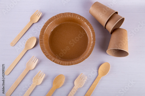Top view on brown carton cups, plate, wooden spoons, forks lay on white table background. Eco tableware concept