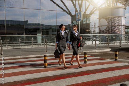 Happy pretty flight attendants with bags crossing the road outdoor