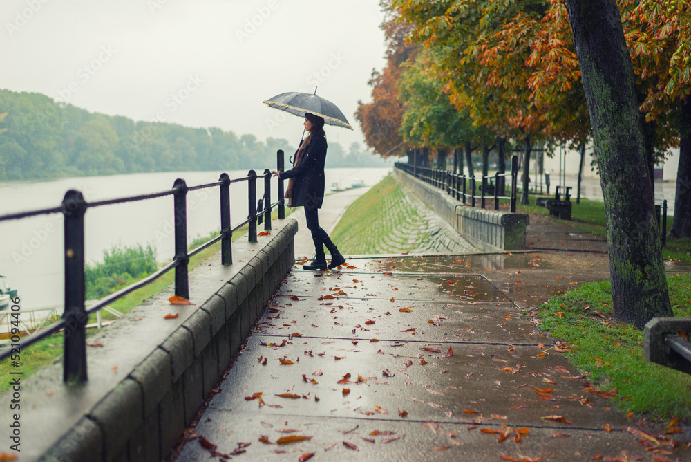Beautiful woman with umbrella walking in the rain on a misty autumn day