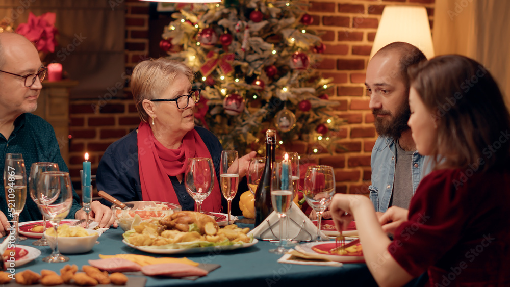 Senior couple talking to married young adults while enjoying traditional home cooked food at Christmas dinner. Festive people celebrating winter holiday with authentic meal and champagne.