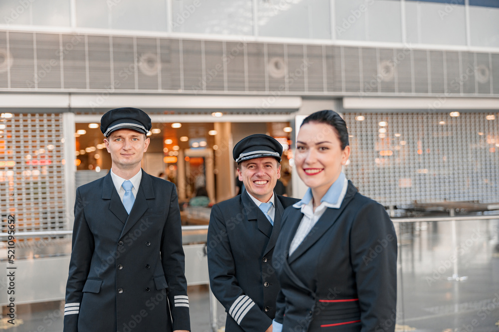 Fototapeta premium Happy two pilots and stewardess standing in the airport terminal