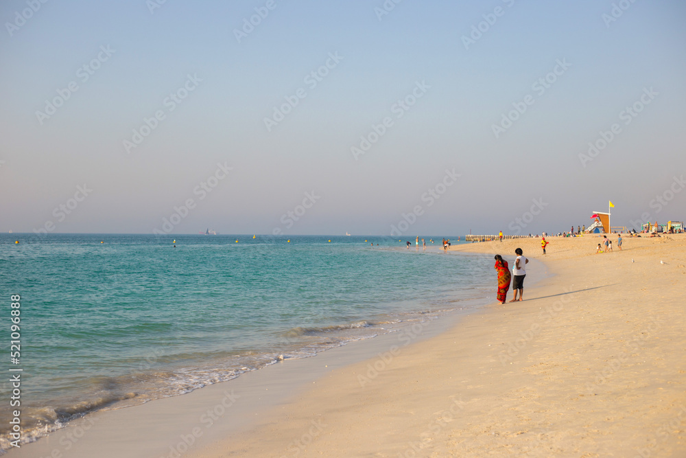 People walk along the beach in Dubai at sunset. Summer walk