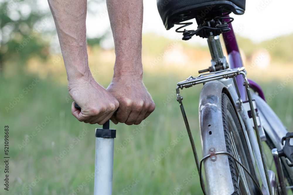 Hands of a man seen pumping a bicycle tire using a stand alone hand pump. Pumping up bicycle tires in the forest on a sunny day. Hands of a man seen pumping a bicycle tire using a stand alone hand pump. Pumping up bicycle tires in the forest on a sunny day.