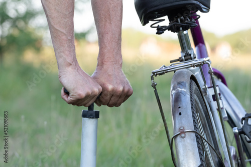 Hands of a man seen pumping a bicycle tire using a stand alone hand pump. Pumping up bicycle tires in the forest on a sunny day.