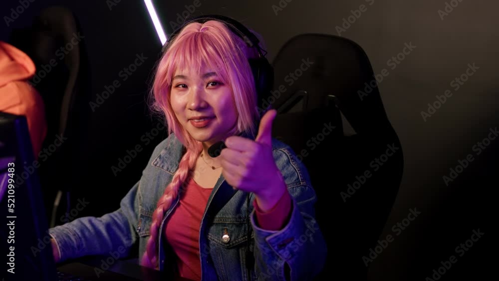 Teenage girl with pink braid using headset competing with her friend in online gaming tournament. Purple lighting. High quality 4k footage Teenage girl with pink braid using headset competing with her friend in online gaming tournament. Purple lighting. High quality 4k footage