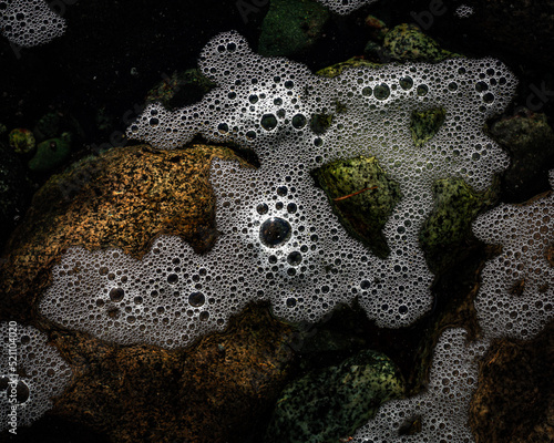 Sea foam scum on ocean water texture with rocks photo