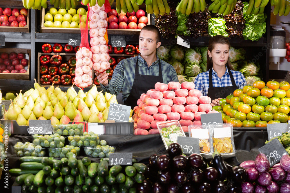 Friendly diligent cheerful smiling man and woman laying out vegetables and fruits in shop